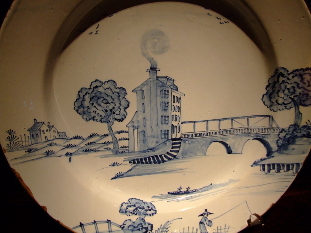 18th century English Delft charger having a blue-gray glaze probably from London depicting a rare subject matter which is asymetrical showing a tower house next to a bridge.  The artist painted with a fine, delicate hand probably by a master