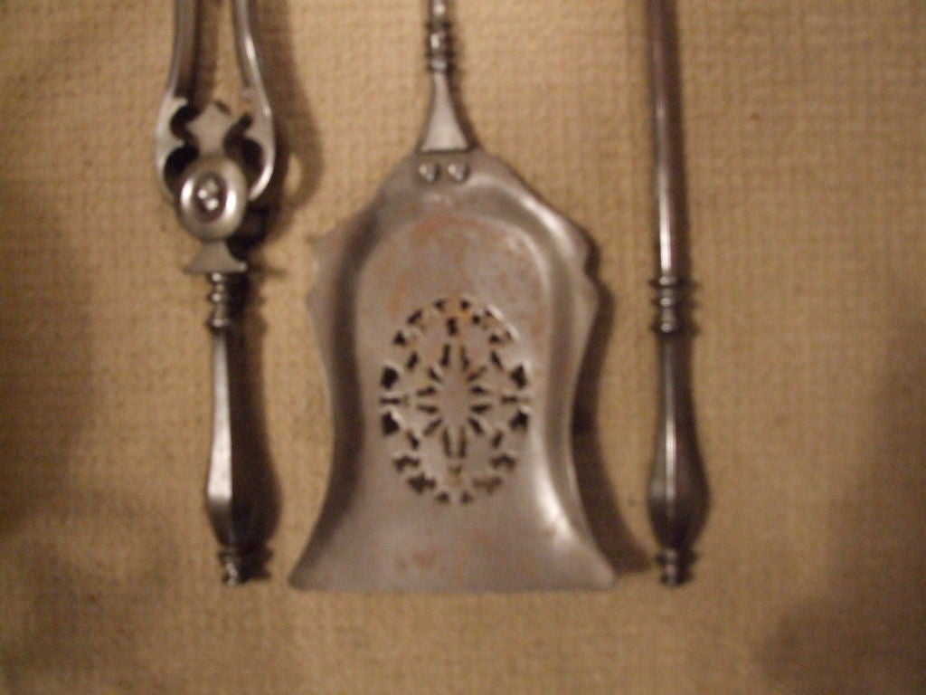 A set of three Regency period English firetools comprising poker, tongs and shovel, in gunmetal steel with oval piercework cut out on shaped shovel bowl.