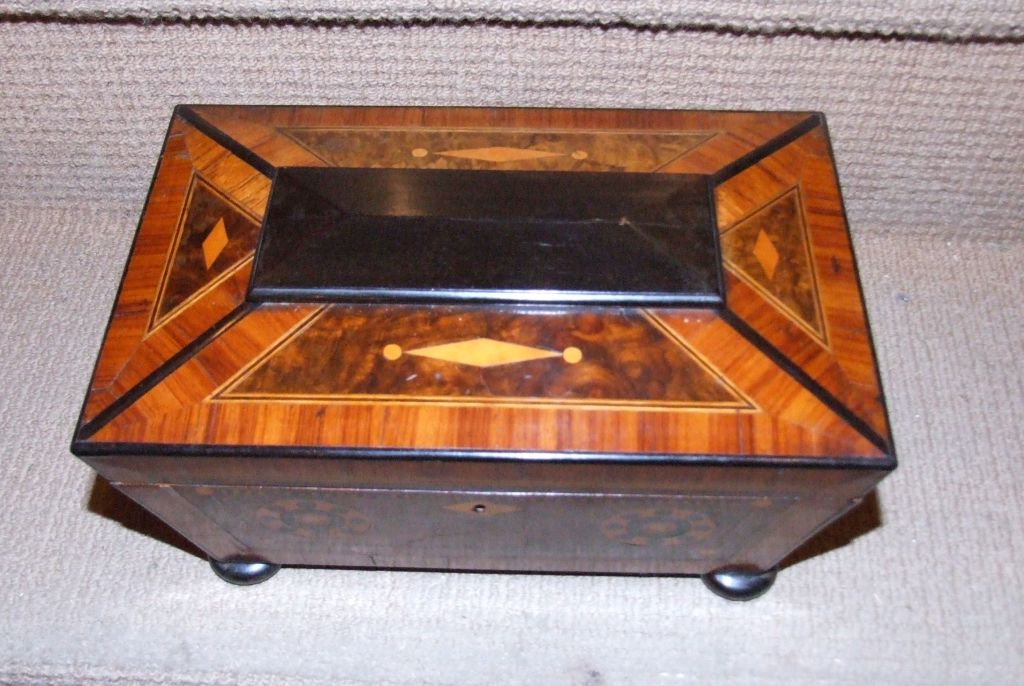 Unusual early 19th Century Welsh tea caddy of sarcophagus form, the canted top with ebony faceted boss, the front having double pinwheel inlay, the top and inner lids inlaid with diamond and bead decoration, containing various woods including ebony,