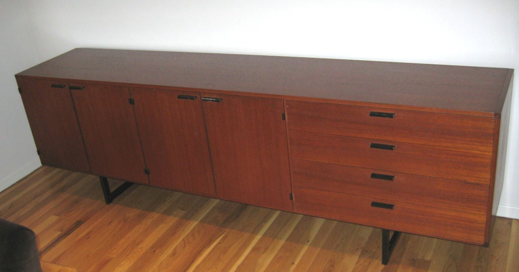 Extremely chic and streamlined credenza in teak veneer with enameled metal pulls and legs. Unit floats on recessed metal sleigh legs. One adjustable shelf in each of the cabinets. Top drawer is felt-lined. Pastoe label in drawer.