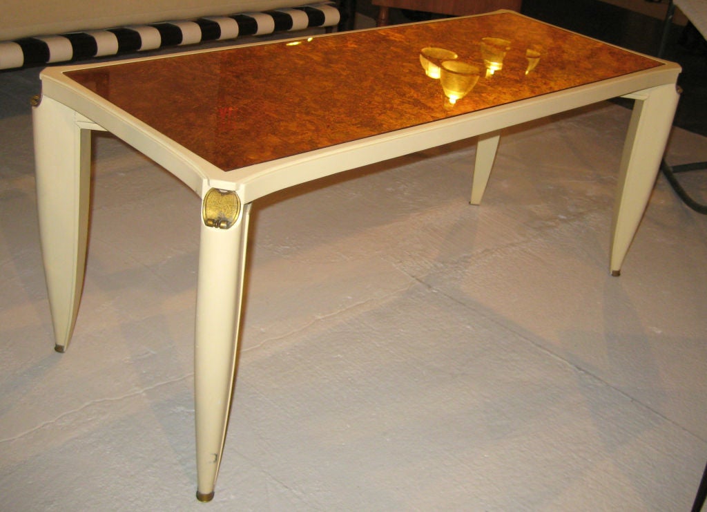 Cream-lacquered table with gilt metal sabots and gold and silver-leafed glass top. Documented.