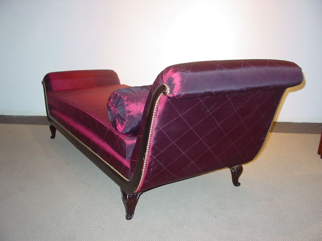 the over-scrolling rectangular headrest with a loose cushion seat and offset footrest in a conforming cove moulded frame on cabriole legs with scroll feet, upholstered in brass tacked burgundy fabric