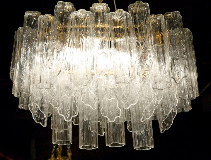 A chandelier consisting of 45 penta foil form clear glass tubes each in a textured, floral-like surface, situated in three oval shaped tiers at varying heights, all mounted to a brass frame by Camer. Italy, circa 1960.