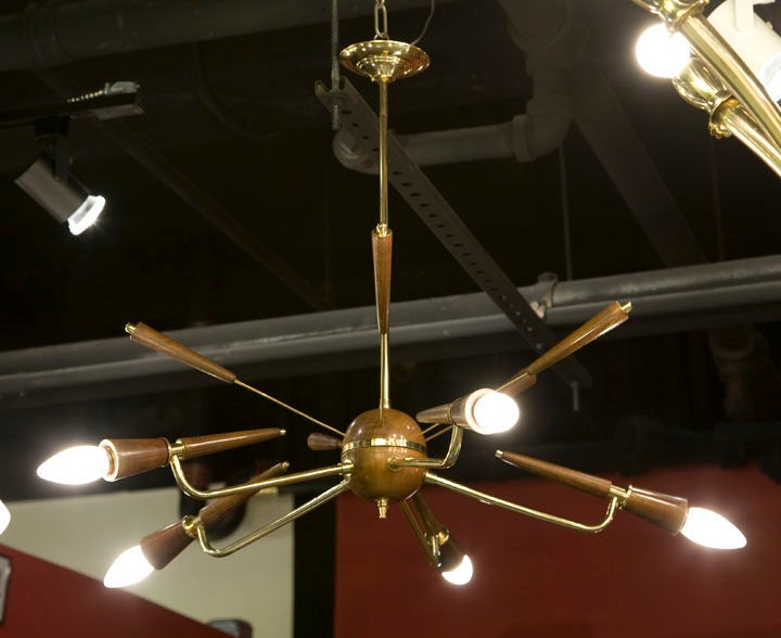 A whimsical “Sputnik” chandelier with brass canopy and pendant that holds a wooden sphere with five brass arms supporting wooden torch shaped forms with bulbs on the lower half and five brass arms supporting wooden torch shaped forms on the upper