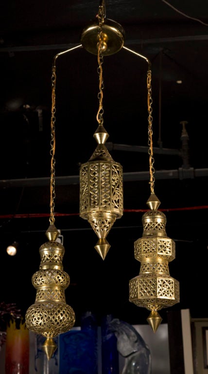 A Moroccan style chandelier with three pierced brass lanterns, each a unique form and suspended on brass chains at varying heights by SarnaLantern (marked). Circa 1960.