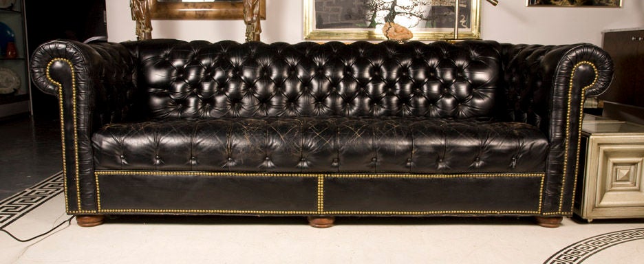 A traditional Chesterfield sofa with tufted black leather, brass studs, raised on bun fee with a fine wear pattern. American, circa 1950.