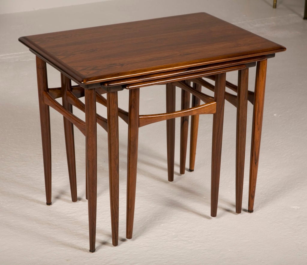 A set of three nesting tables in Rosewood, each with half bullnose edged tops on a simple apron, all resting on four gently tapered legs with three double-splayed stretchers on the larger tables and four on the small table, by Kai Kristensen. 