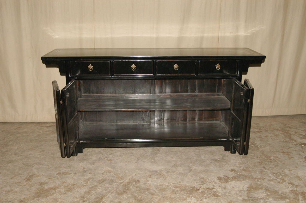 A refined and elegant black lacquer sideboard, with four drawers and a pair of bifold doors, brass fitting, beautiful color, form and lines.