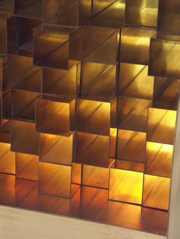A highly imaginative work by Aiko Miyawaki. A brass finished cube, is open to one side and fitted with a grid of 81 square brass tubes. Each tube may be moved to alter its depth in the box and in relation to its neighbors. The cube is lit from the