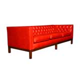 A modern red leather button tufted sofa  on a walnut base