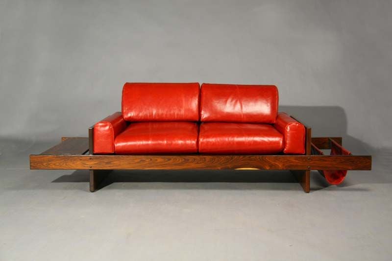 This settee has a leather hanging magazine holder and rosewood side table attached to a beautiful rosewood frame.  The red leather upholstered cushions are new.

Seat depth measures 21