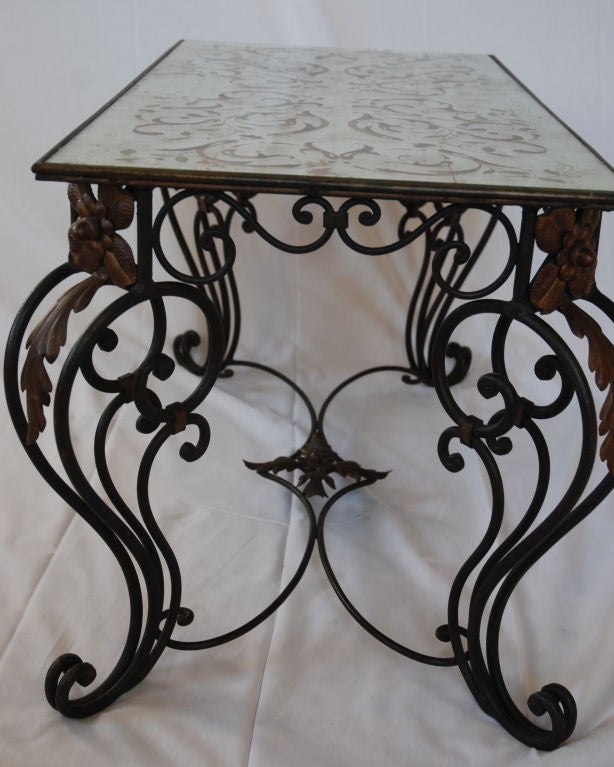Rectangular coffee table with ornate iron legs. Glass top decorated with gold and silver leaf.
