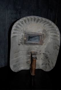 molded mask of heavy weight cardboard with wooden handle.  Looks like metal.