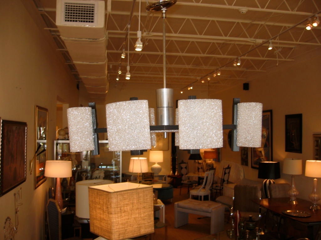 Lampadario composto da acrilico frantumato formato da paralumi ovali che ricordano il vetro sabbioso. Il corpo del lampadario è a forma di diamante in legno nero, mentre gli accessori sono in alluminio e tutti i materiali si completano a vicenda.