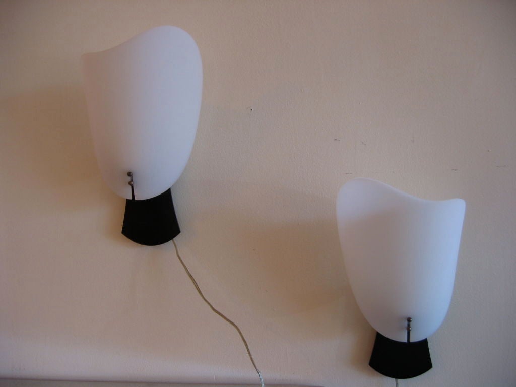 Pair of rewired wall sconces with black painted metal backplates and curved organically shaped white ribbed plastic shades. Small slit on lower portion of shade slides over antiqued brass balls which hold shade in place. Hard wired for wall mounting.