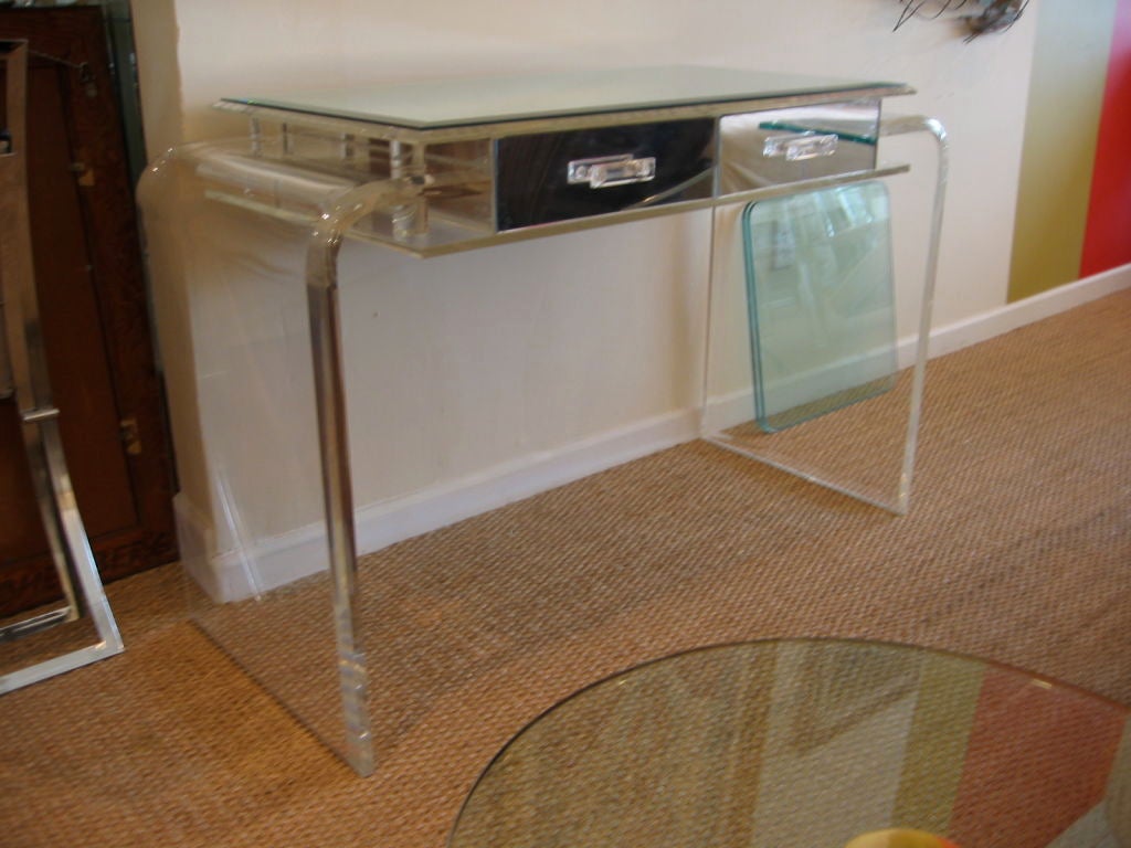 Thick waterfall lucite vanity or desk. Two tiered with two drawers, each mirrored in front, back, and both sides. Lucite handles on both drawers and a beveled mirrored top.
