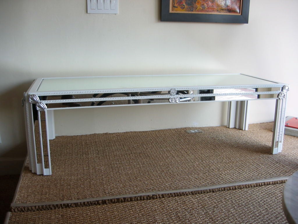 High gloss white lacquered cocktail table with inset mirror strips running along all four sides and on all four legs. Braiding detail surrounding inset strips. Silver leafed resin medallions throughout table. Mirrored top is also inset leaving it