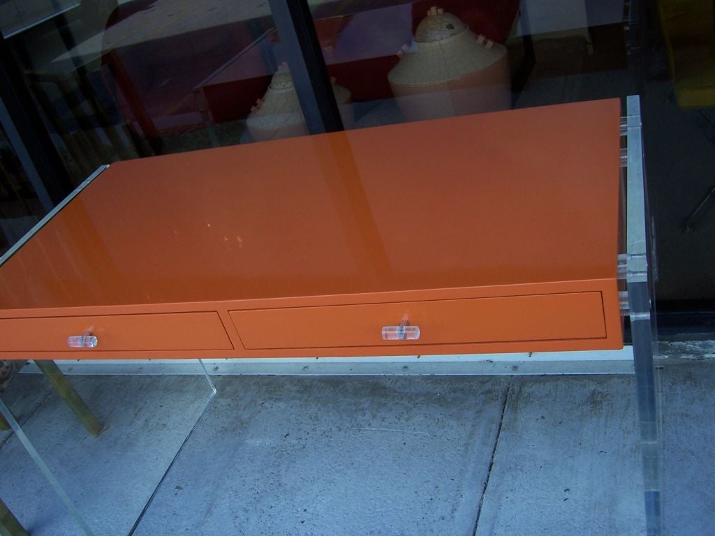 This fantastic modern floating desk in vibrant Hermes orange high gloss lacquer, perfectly refinished.  Two-drawers with original lucite and chrome pulls and lucite panel sides.