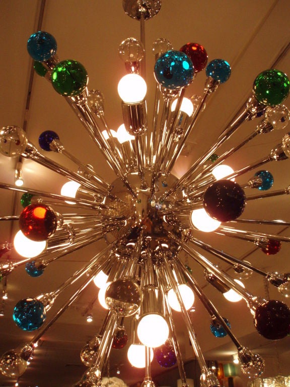 A modernist chandelier featuring a round chrome body with multiple light sources and multiple arms each of which hold a solid glass ball in clear, amber. turquoise, cobalt and green. Italy circa 1960.