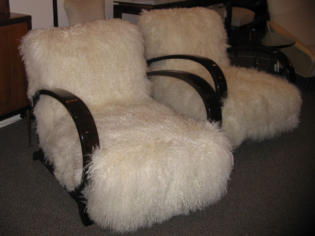 A pair of art deco club chairs featuring frames in polished Mahogany with swooping open arms and splayed legs and all new upholstery in a off white long curly haired Tibetan lamb. Attr. to Jean Royere, France circa 1940. This pair of chairs can be