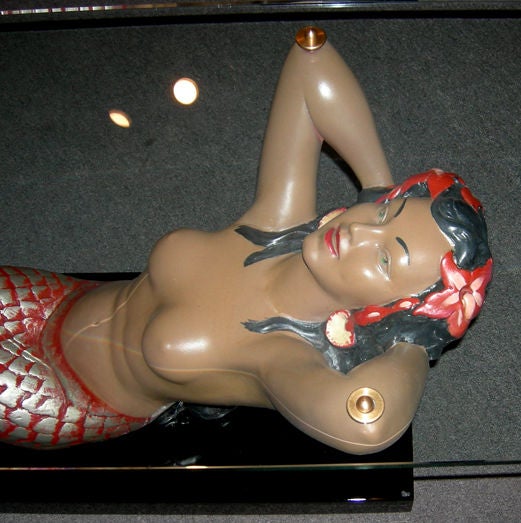 This busty bathing beauty will certainly be the center of attention in any setting. She is painted reinforced plaster, and in excellent restored condition. The base is lacquered wood, and also refinished. A thick, polished glass top is secured by