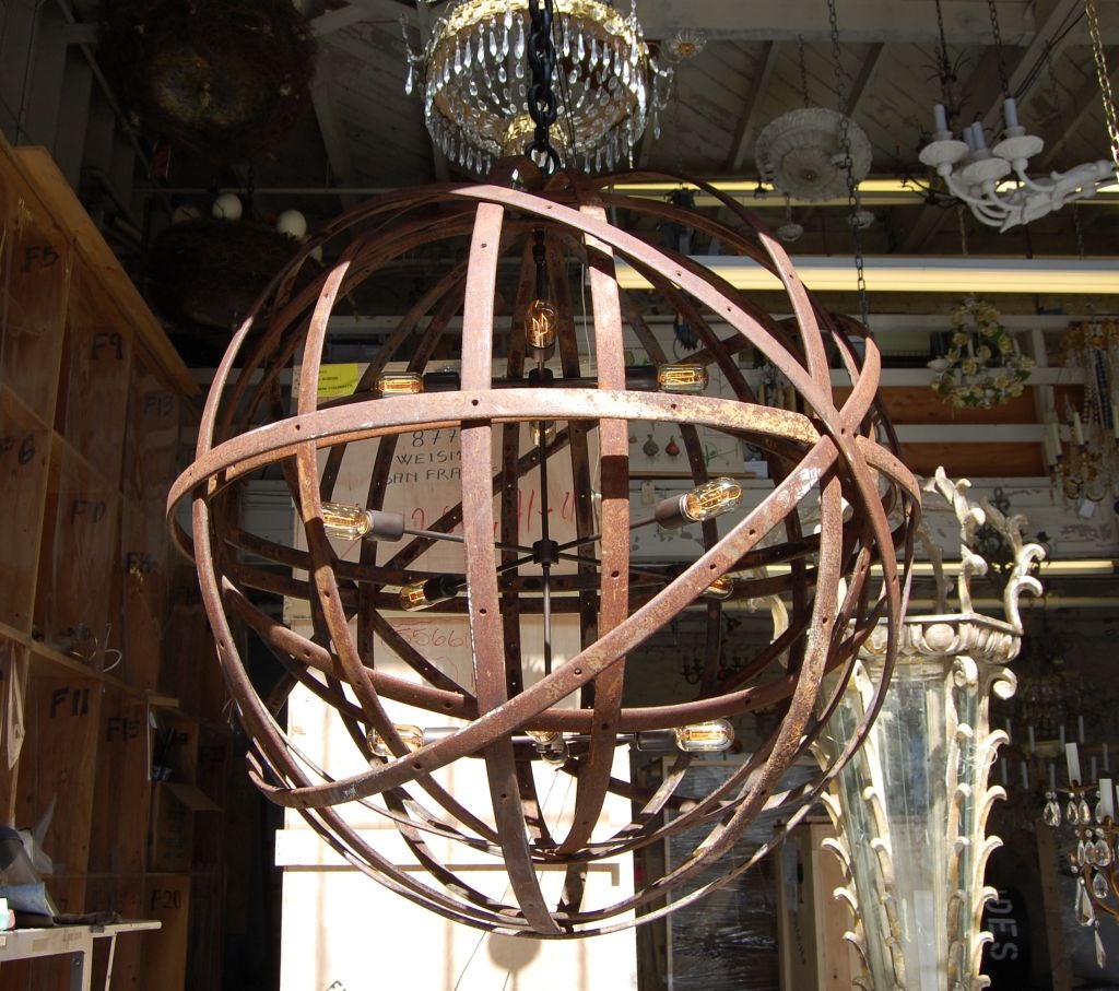 fashionable and contemporary lighting fixture; large rusted metal banding wheels from early 20th Century horse buggies, a sphere welded inside another sphere where the old world meets the brave future 3 illuminated tiers of 4 standard socket lights