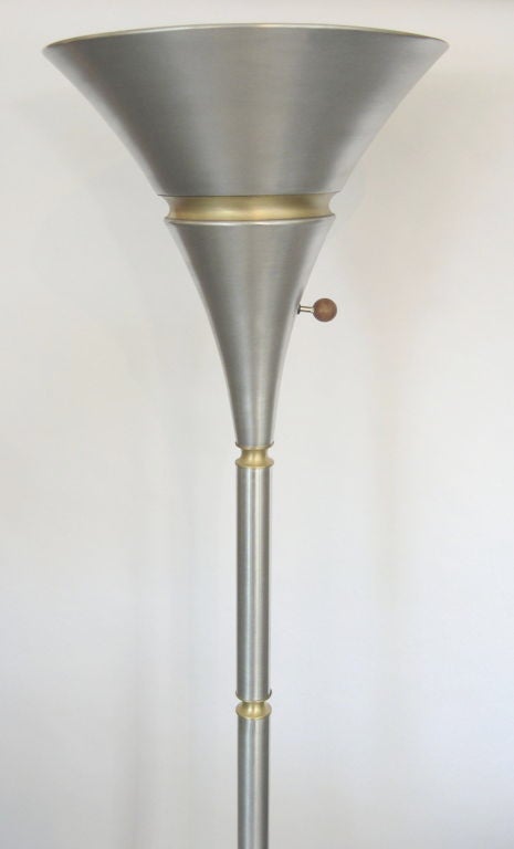 These rare pair of statuesque floor lamps were designed and produced by Russel Wright. The finish is spun aluminum with spun brass accents and base. The three way turn knob is wood. They have mogul sockets and give a lot of indirect light.