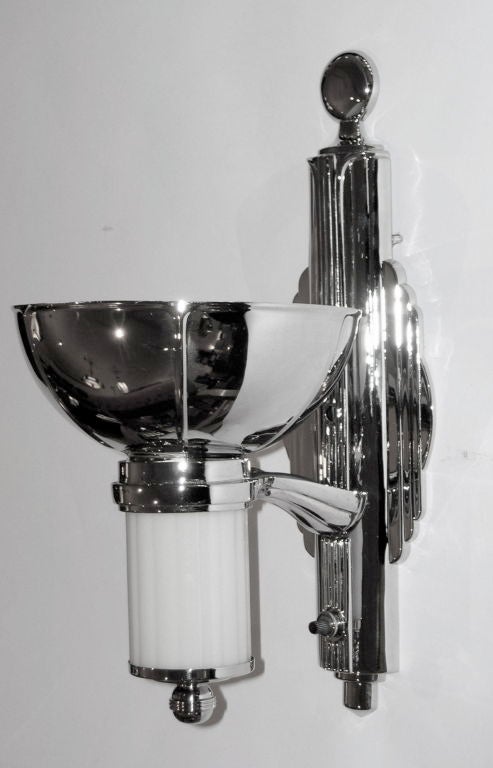 We have 3 pairs available of these rare original sconces available. The are nickel plated brass with molded fluted white glass inserts. When lit, the light is directed upwards and the glass glows. It is difficult to find such a strong art deco