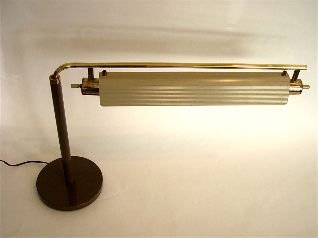 This rare lamp is a table top model designed by Gerald Thurston in 1953 for Lightolier. It's very functional design allows the lamp to adjust in two ways. It has a rotating swing arm with a ribbed metal reflector shade that rotates to angle the