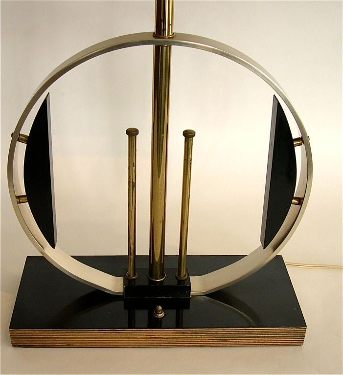 This unique table lamp merges the of best machine age design with the early beginnings of atomic age design. The base is made of early black bakelite laminate 12 ply plywood. The ring is aluminum . The poles are brass and the elliptical accent forms