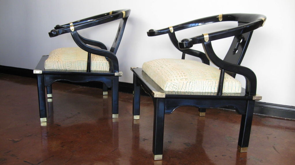 A pair of high gloss black lacquered armchairs in th manner of James Mont. They have traditional Asian elements with brass accents. Seats are upholstered in faux crocodile leather. Seat height is 17 inches.