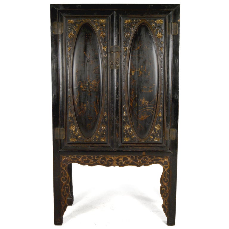 An ornately detailed early 20th century Chinese cabinet with oval relief paneled doors painted with landscape scenes, on highly carved legs with gilt scrolling vines, and an interior with three shelves and three drawers with brass hardware.<br