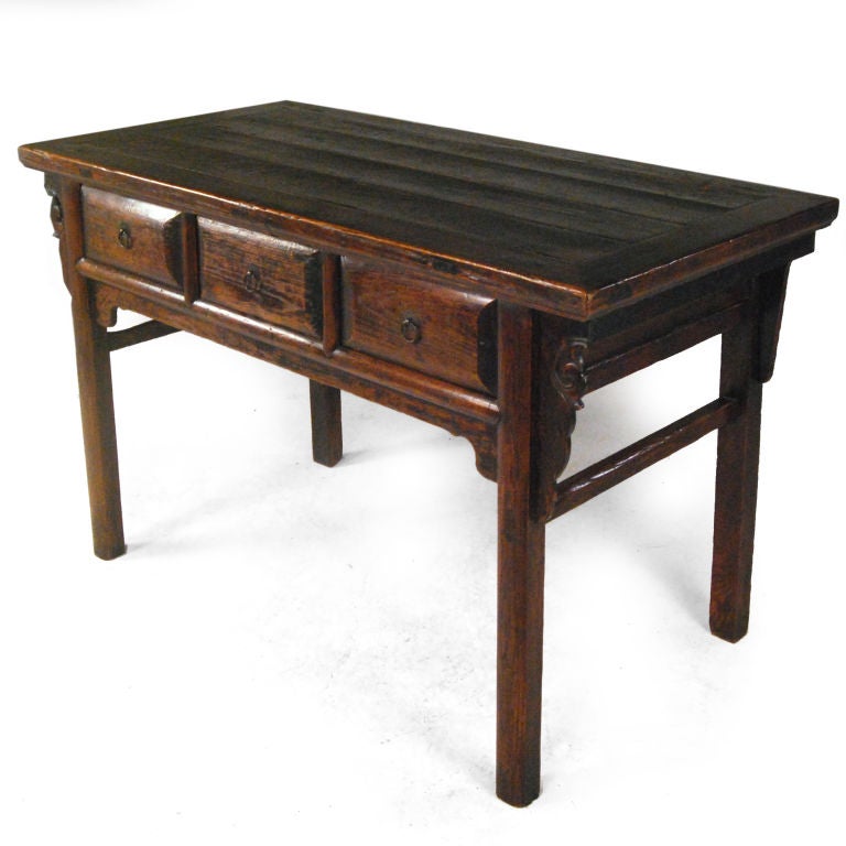 A provincial Chinese elmwood table with carved floral spandrels, and three drawers with brass hardware.<br />
<br />
Pagoda Red Collection #:  GDI012<br />
<br />
<br />
Keywords:  Table, desk, night stand, bedside, console