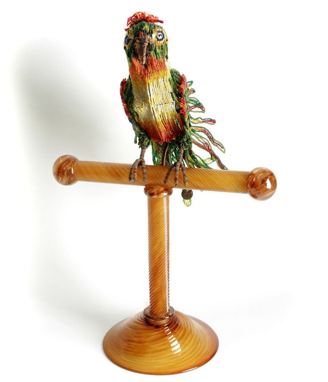 This  hand beaded parrot sits atop a golden perch of murano glass.  The color of the glass takes on a wood like quality. I have only seen beaded pieces mounted on blocks of wood.  The beading is very intricate and well done.  The lamp retains it's
