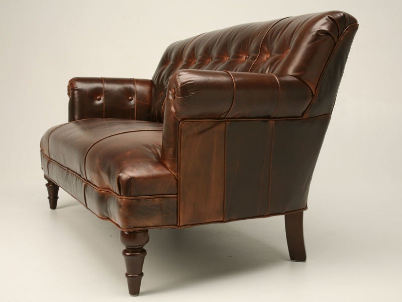 Reproduction tufted back leather settee with rolled arms and turned, tapered legs.