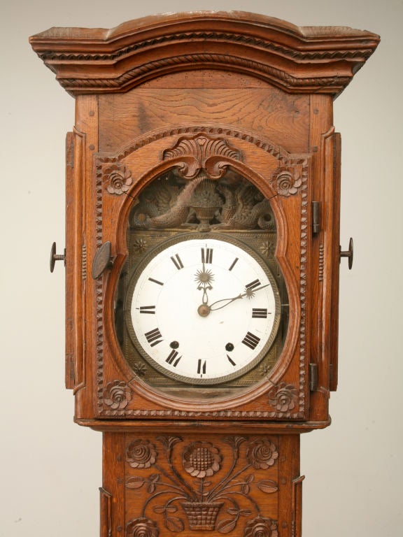 Outstanding antique Normandy region Country French tall case clock hand-carved from oak with hand-forged hardware, wooden-peg construction, original wavy glasses, a porcelain clock face and all around magnificent detailing. Interesting original