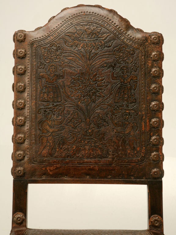 Spectacular antique Spanish oak and original tooled leather desk chair in fantastic condition. This exquisite chair has a fantastic hand-carved Bacchus-form relief stretcher, a camel back, and unique flora-form nails, to boot.