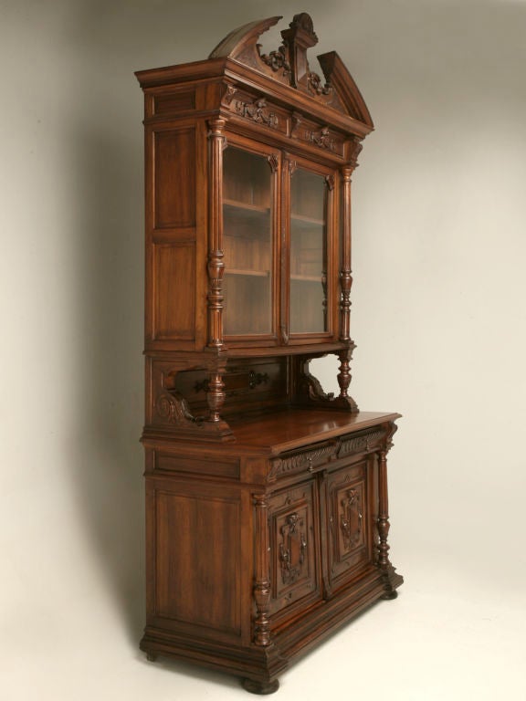Exquisite! Renaissance Revival (Henri II) ornately carved walnut cupboard with original wavy glass upper doors. Embellished recessed panels have draping banners and scrollwork with flared leaves and hanging bell-flowers adorning the frieze. Fluted