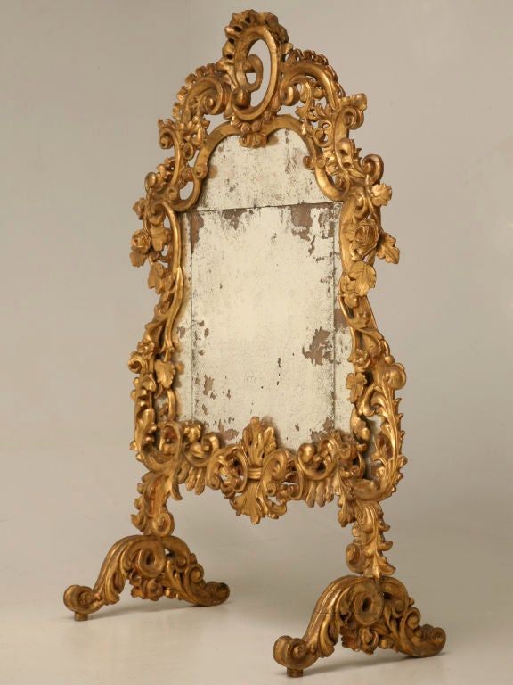 Antique Italian mirrored fire screen with intricate foliate hand-carved gilt wood frame. One of the most beautiful 18th century Italian gilt mirrors we've ever had. With some work, our shop could remove the feet leaving you an exquisite unparalleled