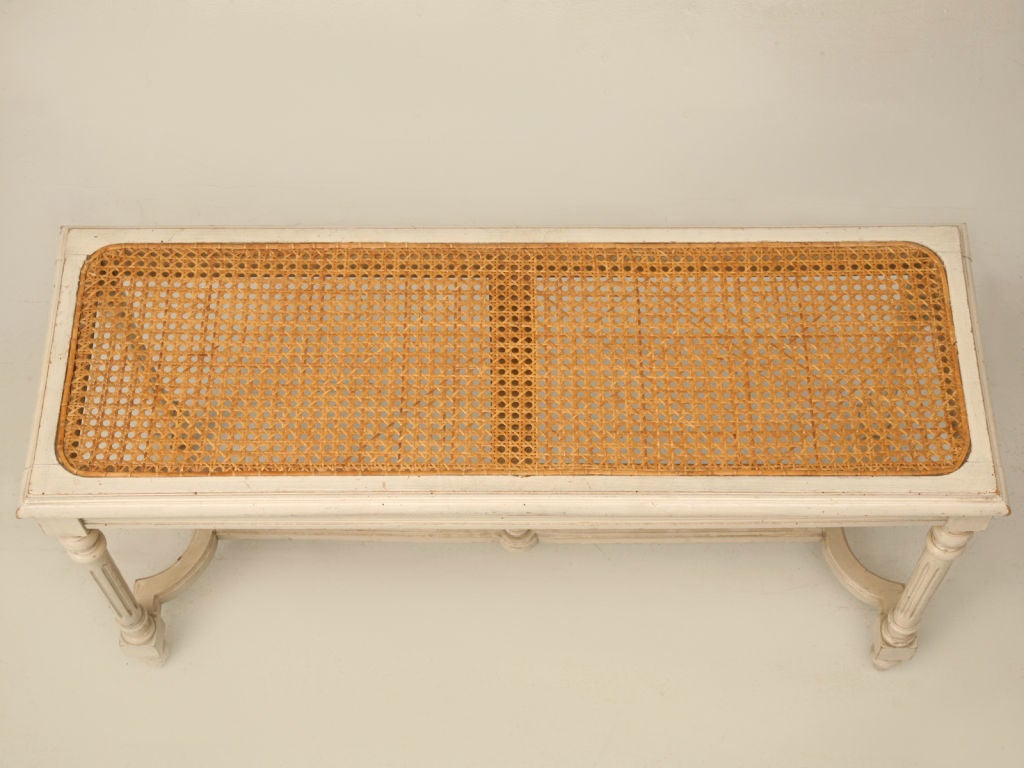 Vintage painted Louis XVI style bench with a caned seat and a great stretcher with finial. This bench would be welcoming in most any room of ones home, be it the entry-hall, at the foot of the bed, or even as a versatile small coffee table in a