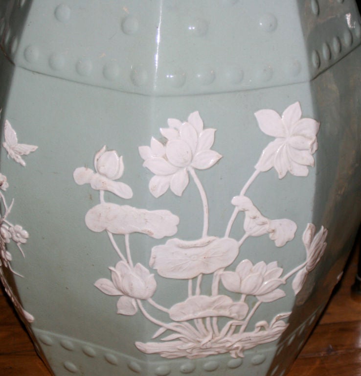 A celadon colored Chinese porcelain garden stool with cream colored floral decoration and raised dots. The top having a pierced fret cutout.