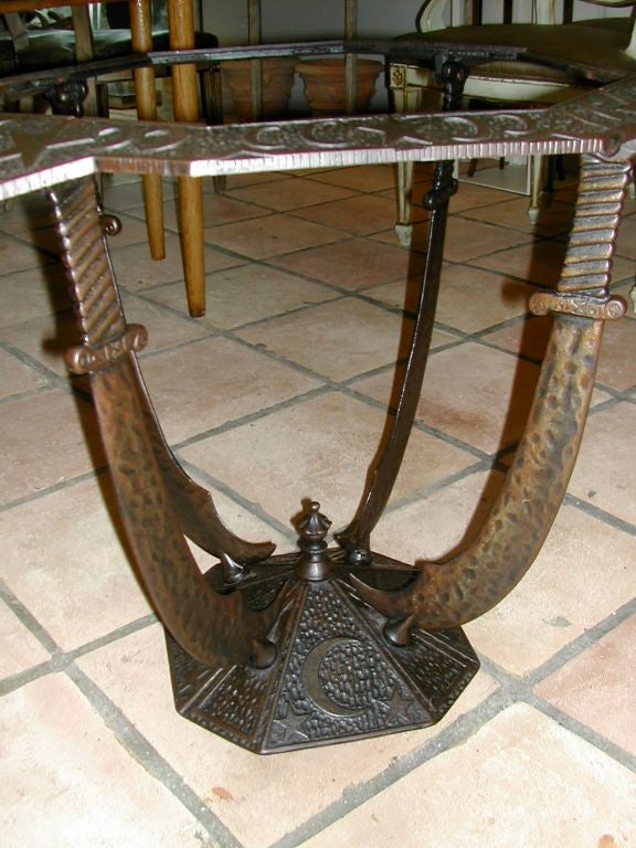 OCTAGONAL SHAPED CAST IRON TABLE WITH GLASS INSERT TOP. THIS TABLE WAS MADE BY THE SEVILLE STUDIOS, CLEVELAND. THE MOTIF CONSISTS OF STARS, MOON AND SABERS. PROBABLY FROM A MASONIC-SHRINERS LODGE HALL.