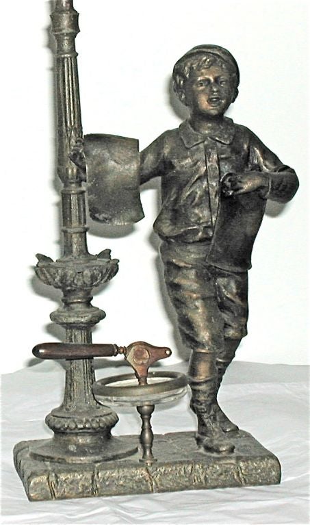 Patinated metal figure of newsboy mounted on countertop cigar cutter.The hurricane at the flame is glass(probably a somewhat later replacement).