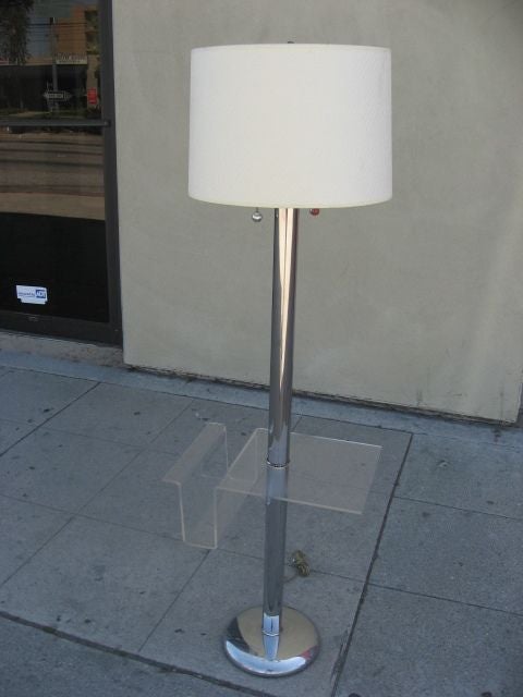 Modern chrome floor lamp with rounded bottom.  String pulls to switch on two bulbs.  Lucite shelf with magazine rack attached to center of lamp base.  Very unique.