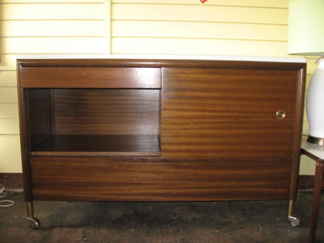 This on wheels walnut credenza has a white formica top and hides on each side 2 occasional folding tables very practical to have dinner seating on your couch.