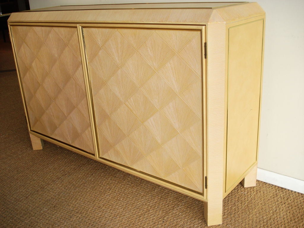 2 doors cabinet, wrapped in leather with brass trim. Doors have fan shaped patterns imitating straw marquetry.
