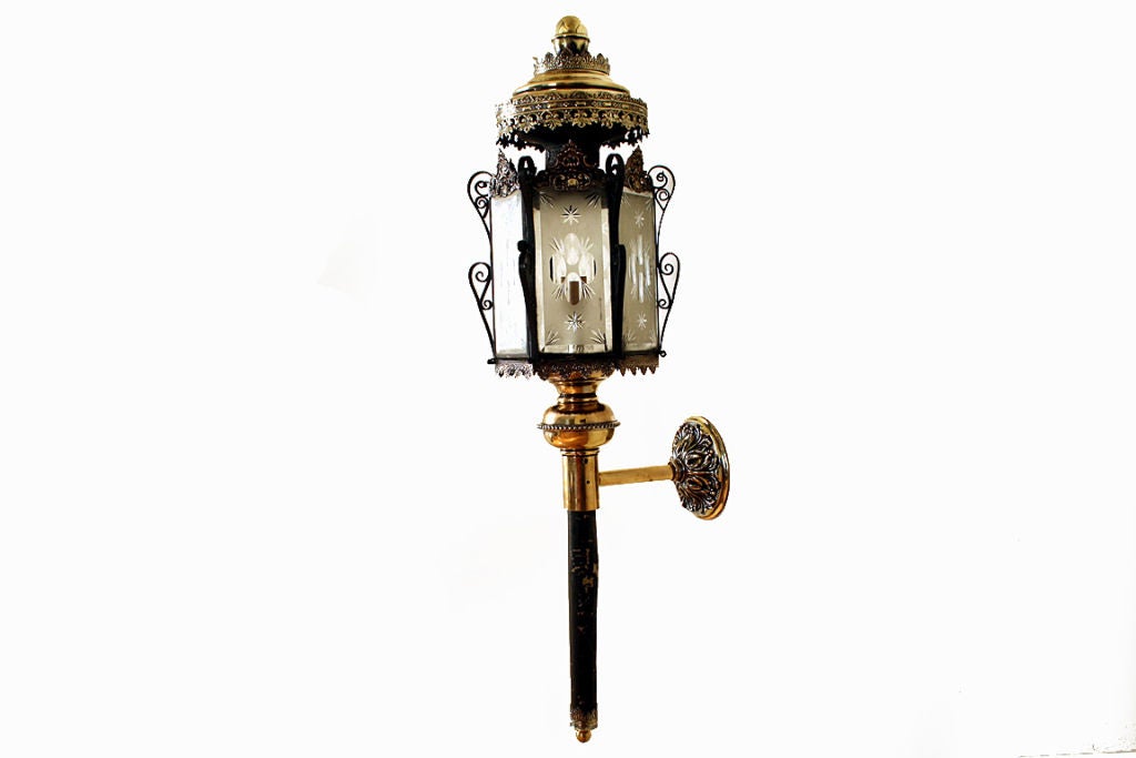The brass ball finial atop a tapering roof with pierced brasswork surrounds atop a hexagonal body with origiginal etched glass panels containing a single light, continuing to an ebonized metal torchere base, attached to the wall by a brass post and