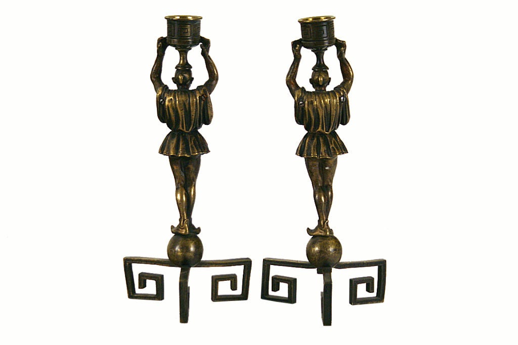 In the oriental style, each candlestick depicting a servant in flowing dress holding a Greek key cast candle cup above his head, with upturned slippers standing atop globes resting on a tripartite Greek key base

