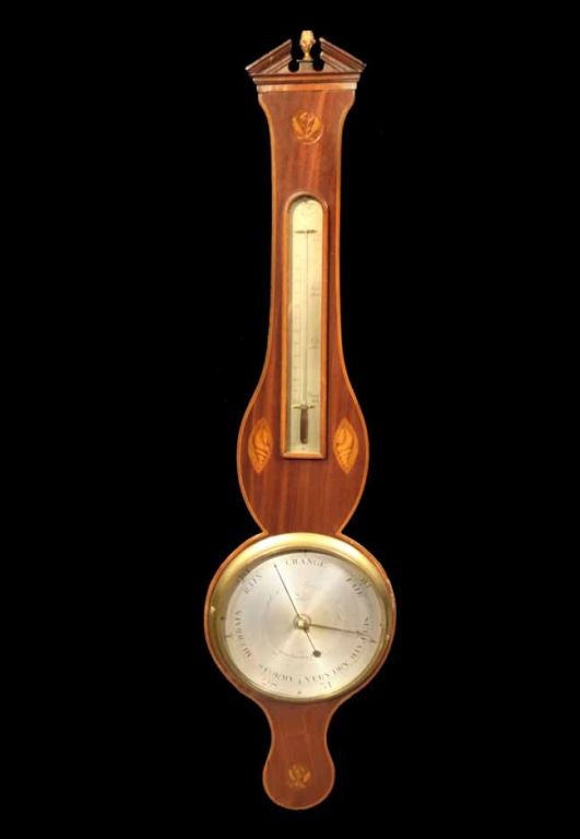 # S155 - Fine George III mahogany wheel barometer. The broken arch pediment is above a finely detailed frieze above a boxwood leaf motif. The vase-shaped top centers a silvered thermometer flanked by decorative shell inlay. The silvered wheel