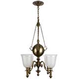 A four-arm brass chandelier with hurricane shades